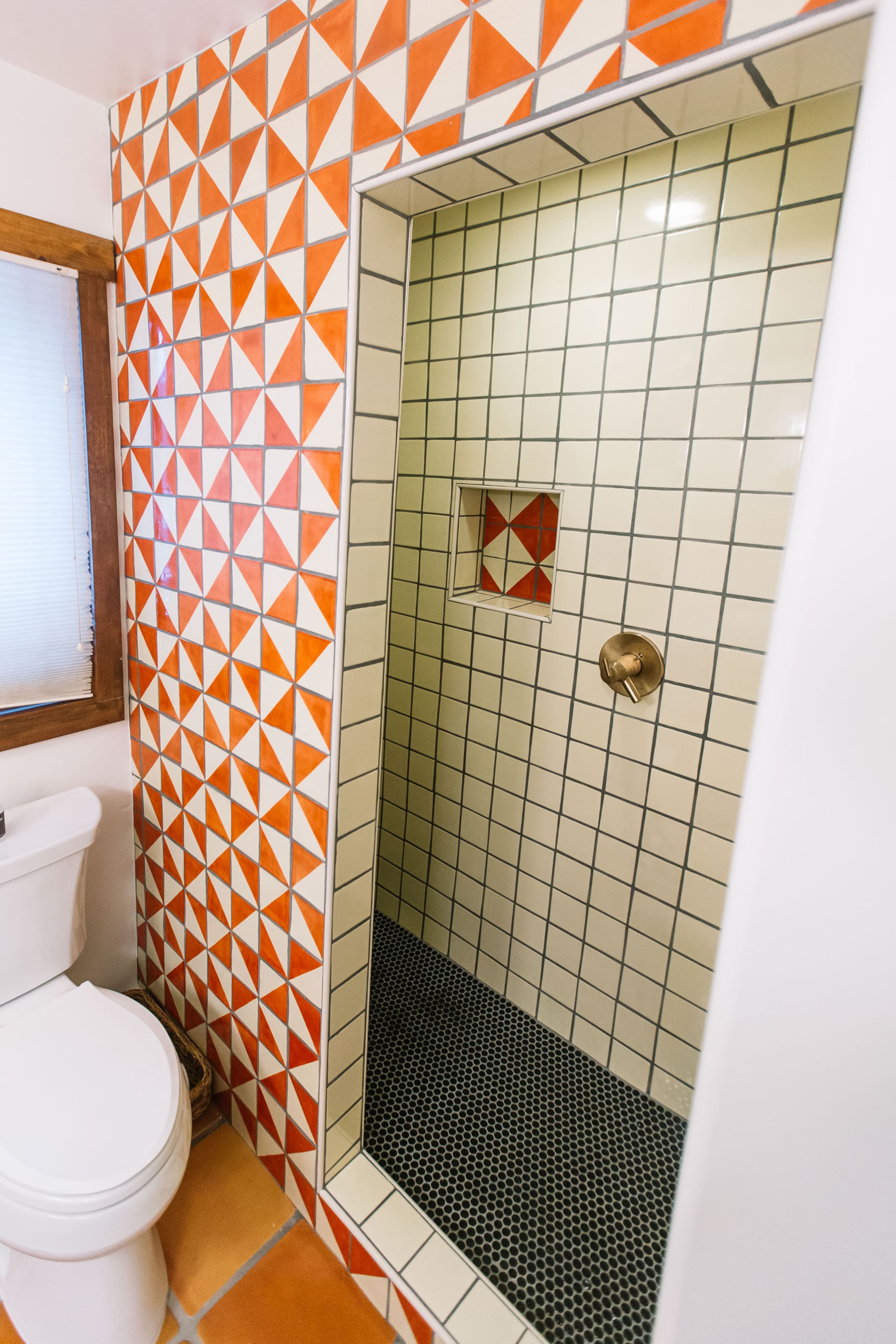 Orange triangle-tile shower with penny-tile floor and brass fixtures