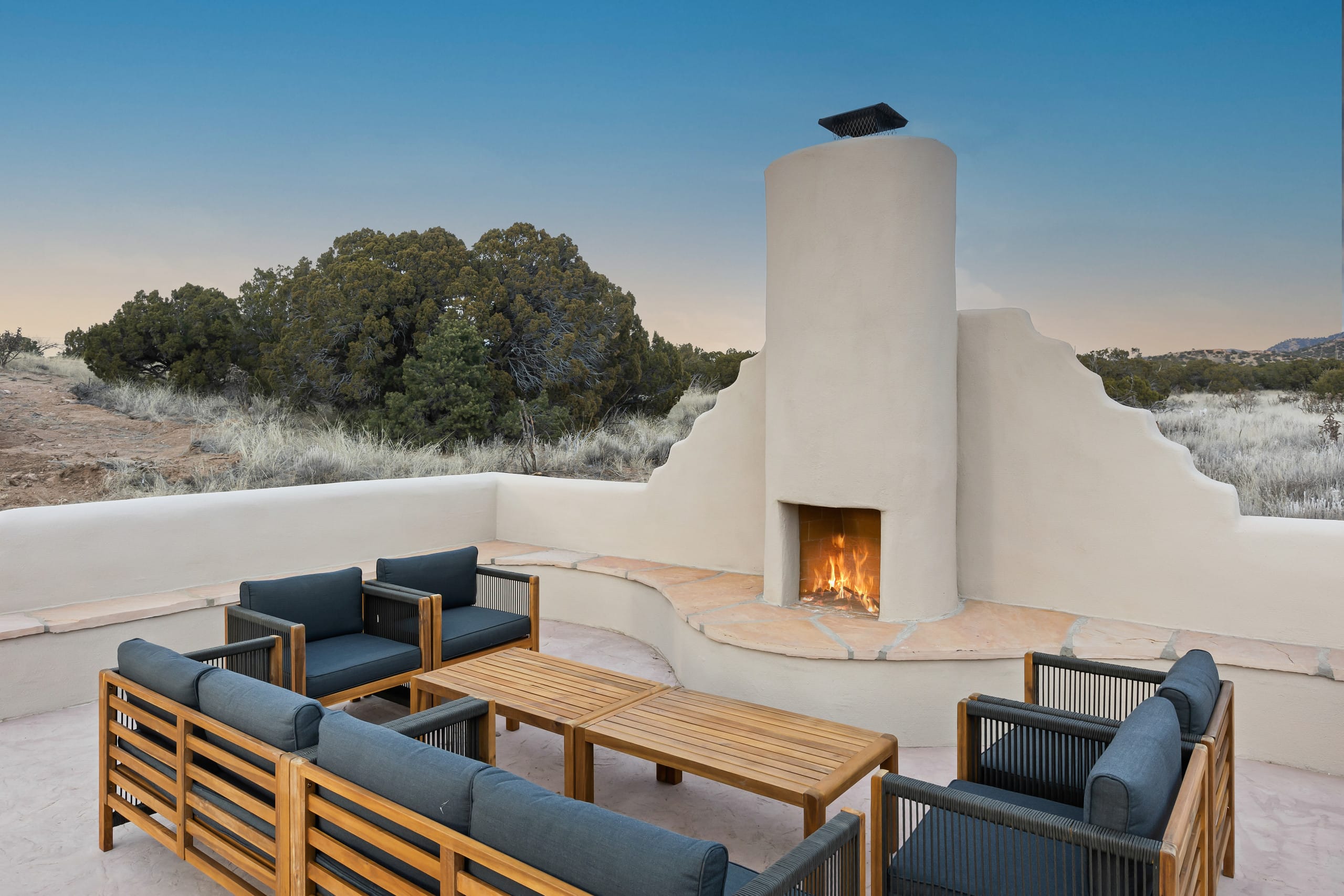 Outdoor kiva fireplace lit at dusk with lounge seating