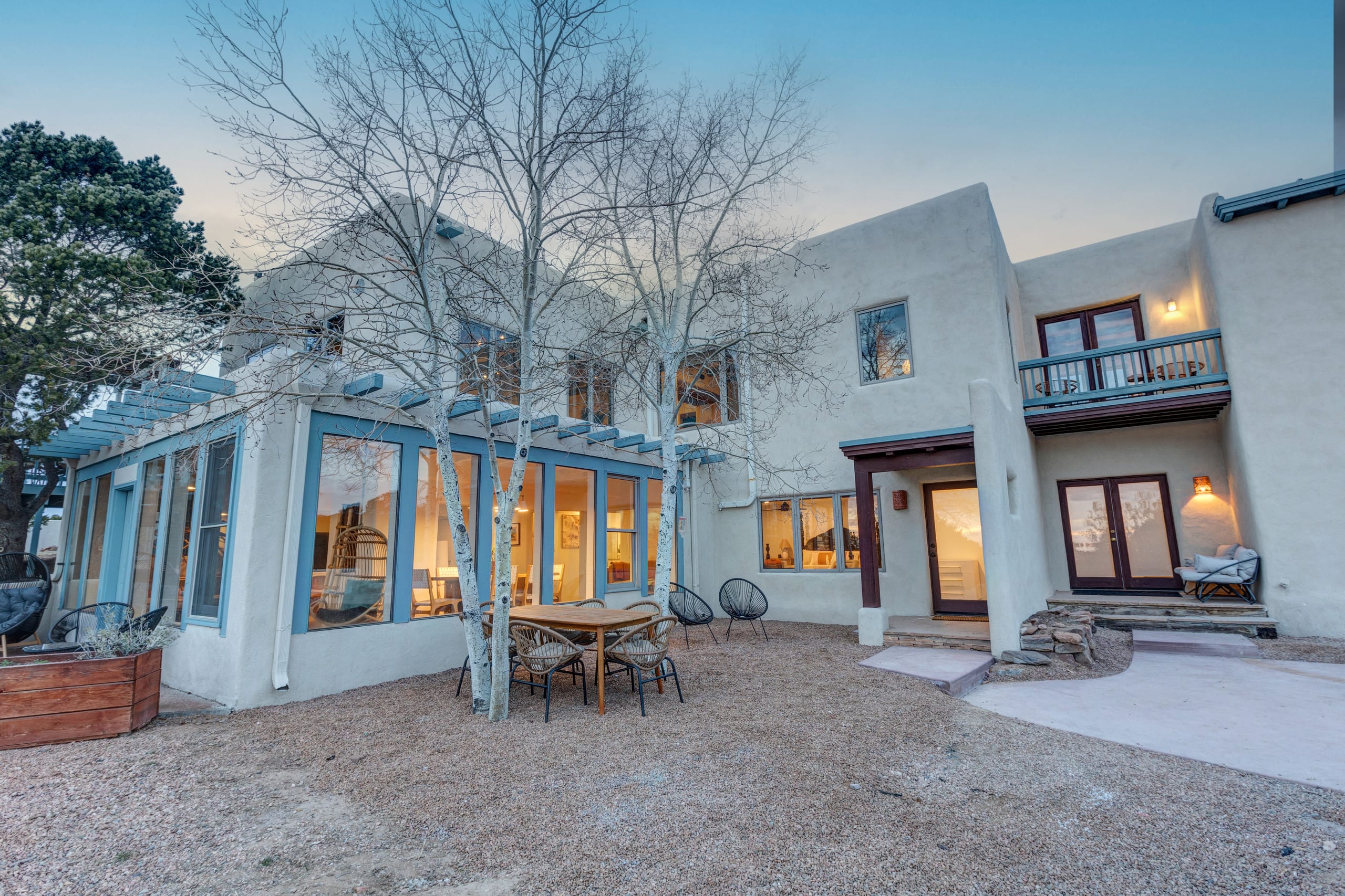Glowing sunroom and guest wing through bare aspens at dusk