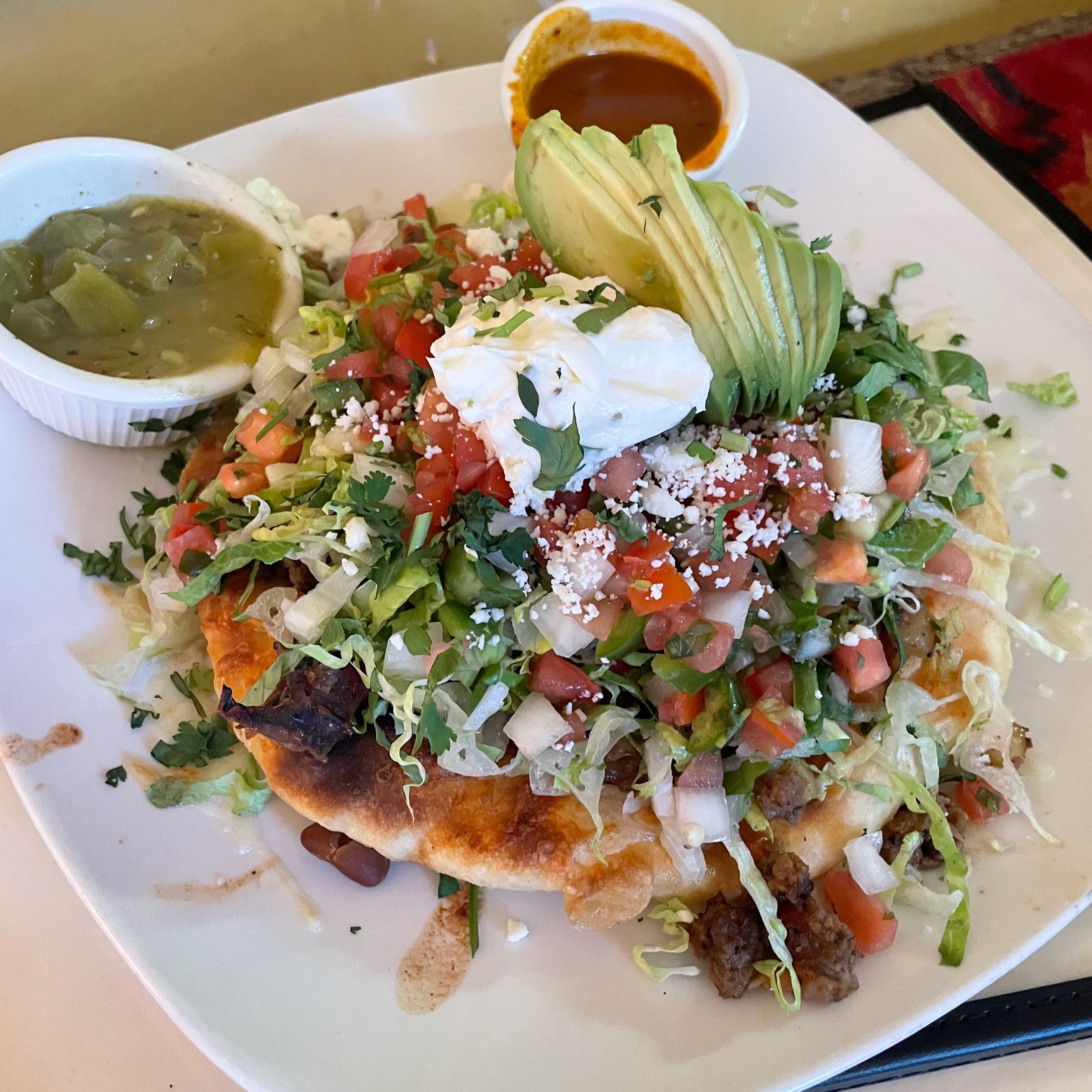 A Navajo taco on frybread piled with beef, lettuce, pico, cotija, and fanned avocado at Casa Chimayo