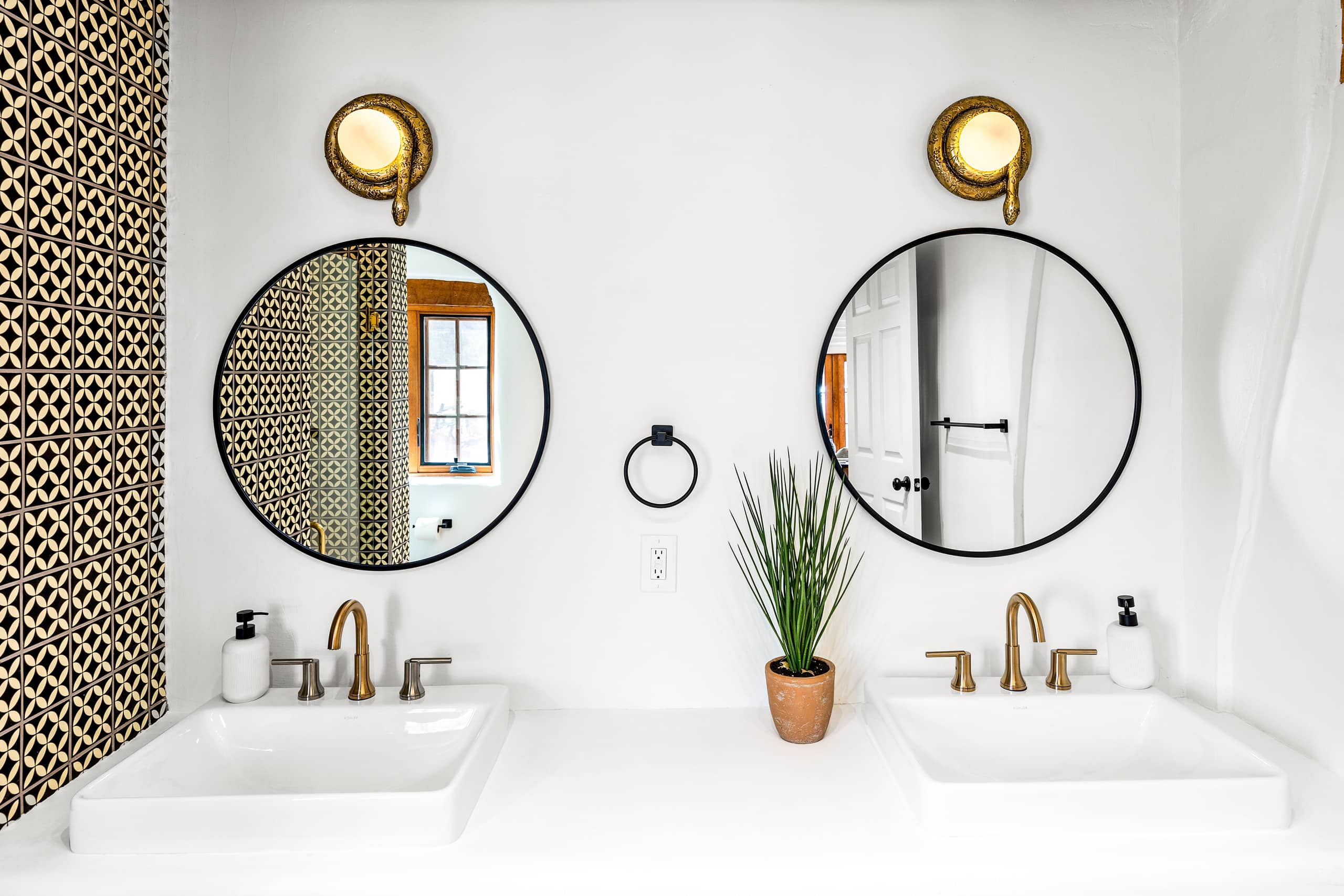 Bath with double vessel sinks, round mirrors, and brass sconces